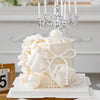 A white tiered cake decorated with sheer fabric petals and pearl accents, topped with an ornate silver candelabra.