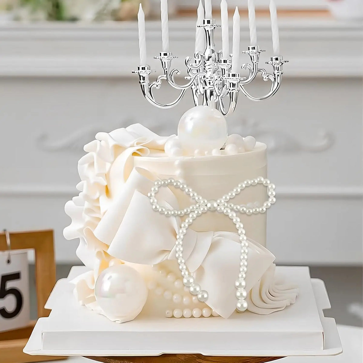 A white tiered cake decorated with sheer fabric petals and pearl accents, topped with an ornate silver candelabra.