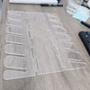 A clear acrylic cap storage rack with multiple display slots is shown on a wooden surface.