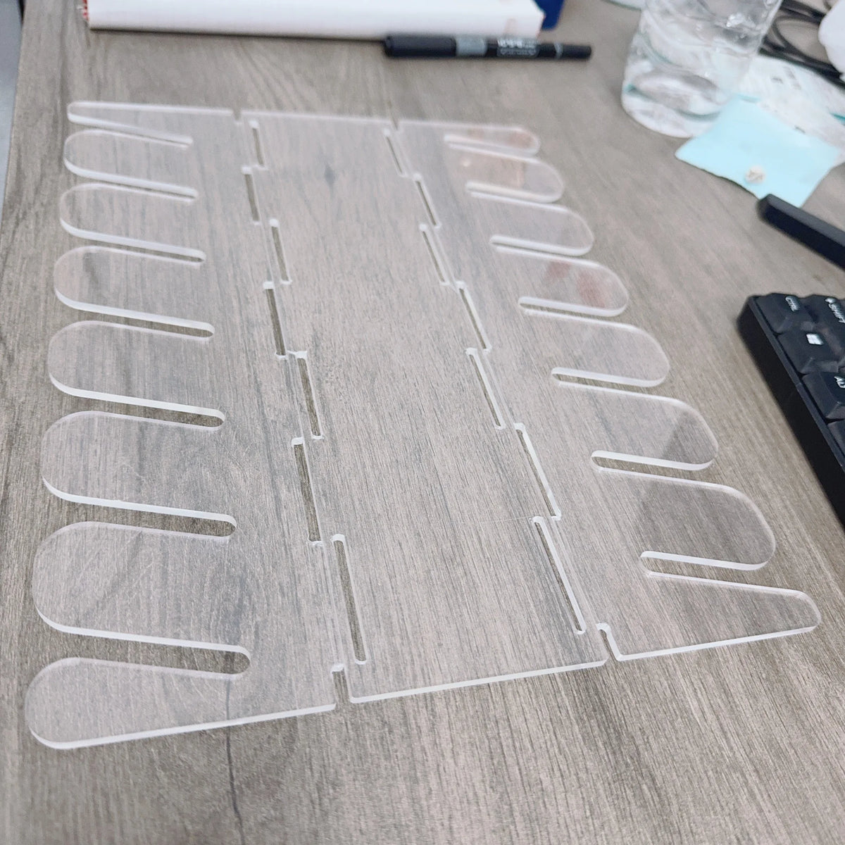A clear acrylic cap storage rack with multiple display slots is shown on a wooden surface.