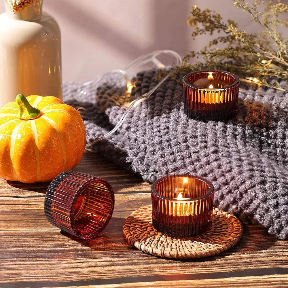 Gold glass tealight candle holders resting on a woven mat and dark gray knitted fabric.