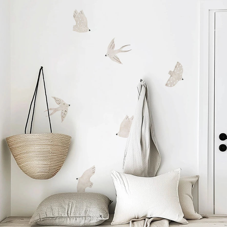 Sammlung abnehmbarer Cartoon-Vogel-Wanddekals auf weißer Wand über einem geflochtenen Pendelleuchte und Kissen.