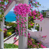 A vibrant pink artificial violet ivy hanging garland cascades from a pergola, set against a blue sea view.