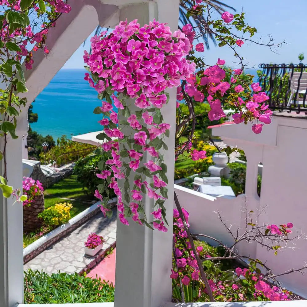 A vibrant pink artificial violet ivy hanging garland cascades from a pergola, set against a blue sea view.