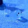 A translucent blue glow in the dark resin sea animal figurine with a cat face, shown against a blue glitter background.