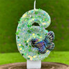 A large number six candle decorated with green and iridescent sequins, featuring a butterfly design.