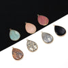 A collection of oval gemstone pendants in shades of pink, green, gray, and black set against a dark background.