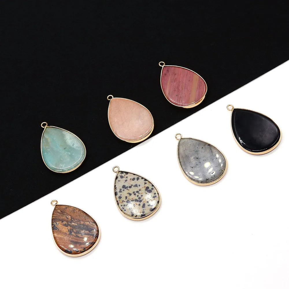 A collection of oval gemstone pendants in shades of pink, green, gray, and black set against a dark background.