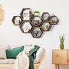 A set of four wooden hexagon floating shelves displaying various small decorative items and clocks on a white wall.