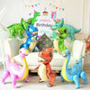 A collection of colorful dinosaur-themed balloons and film decorations arranged on a white sofa.