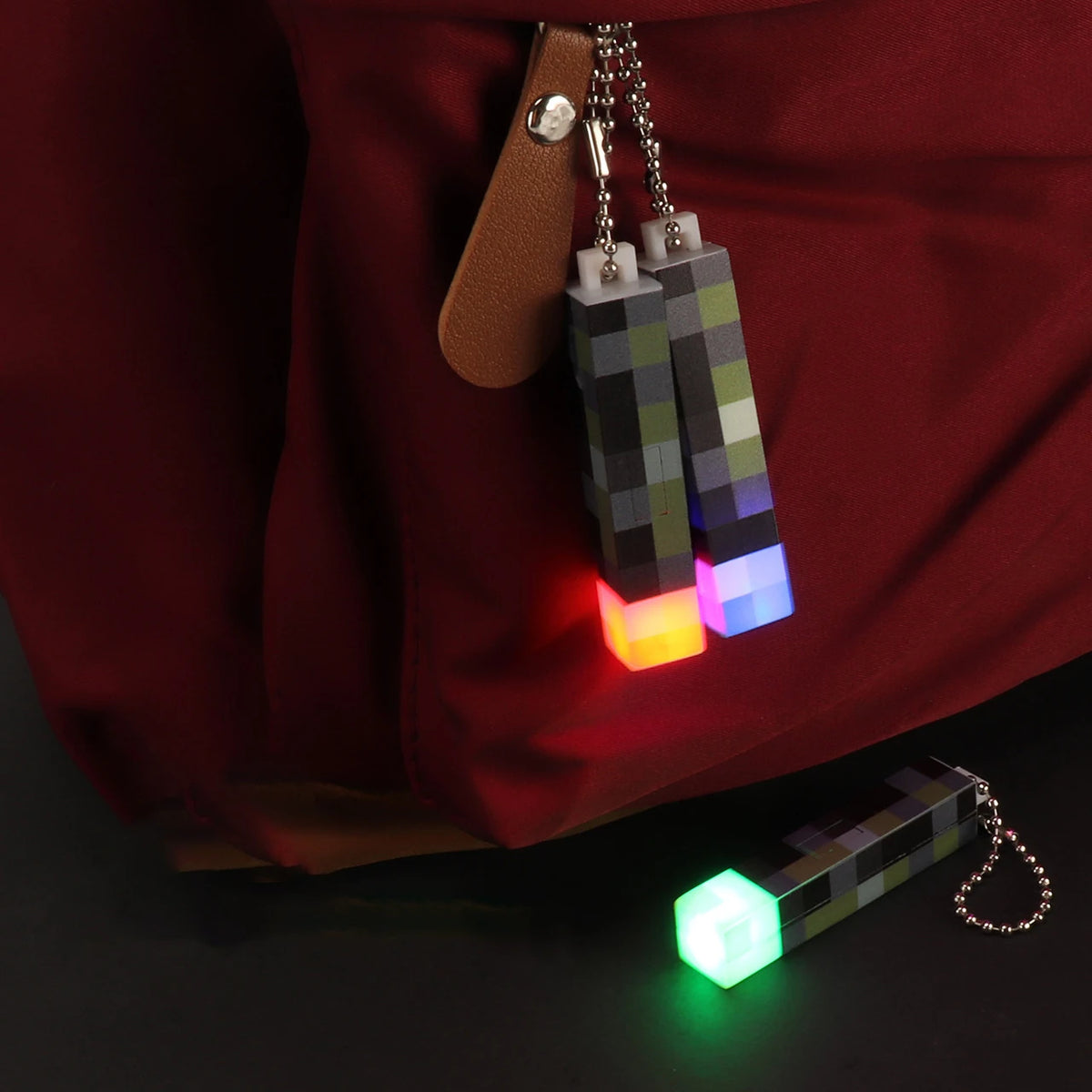A set of pixel art mini flashlights with glowing LEDs hanging from a leather strap against a dark background.