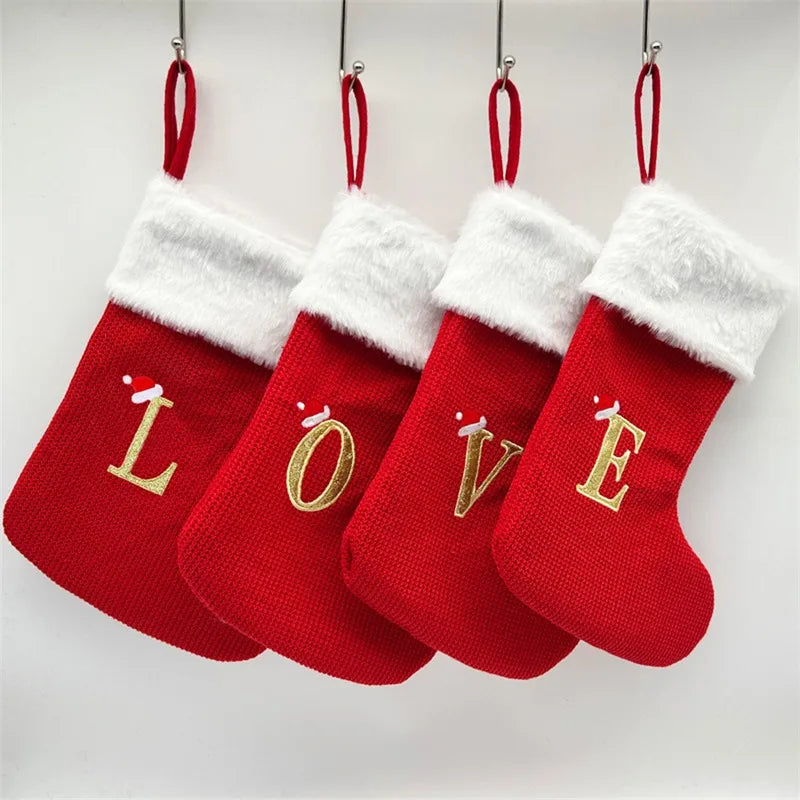 A set of red Christmas alphabet knitting socks with gold letters hanging on a white background.