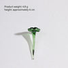 A small, translucent green glass flower with a stem and leaves casting a shadow on a white surface.