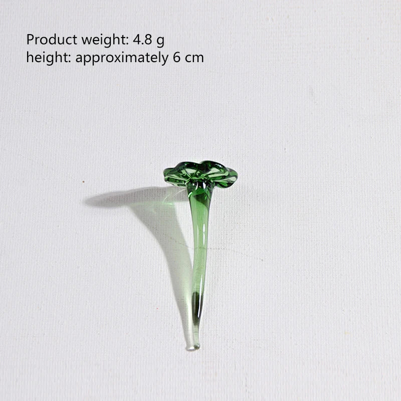 A small, translucent green glass flower with a stem and leaves casting a shadow on a white surface.