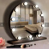 A round dimmable LED vanity mirror reflecting a bedroom and a makeup brush on a table.