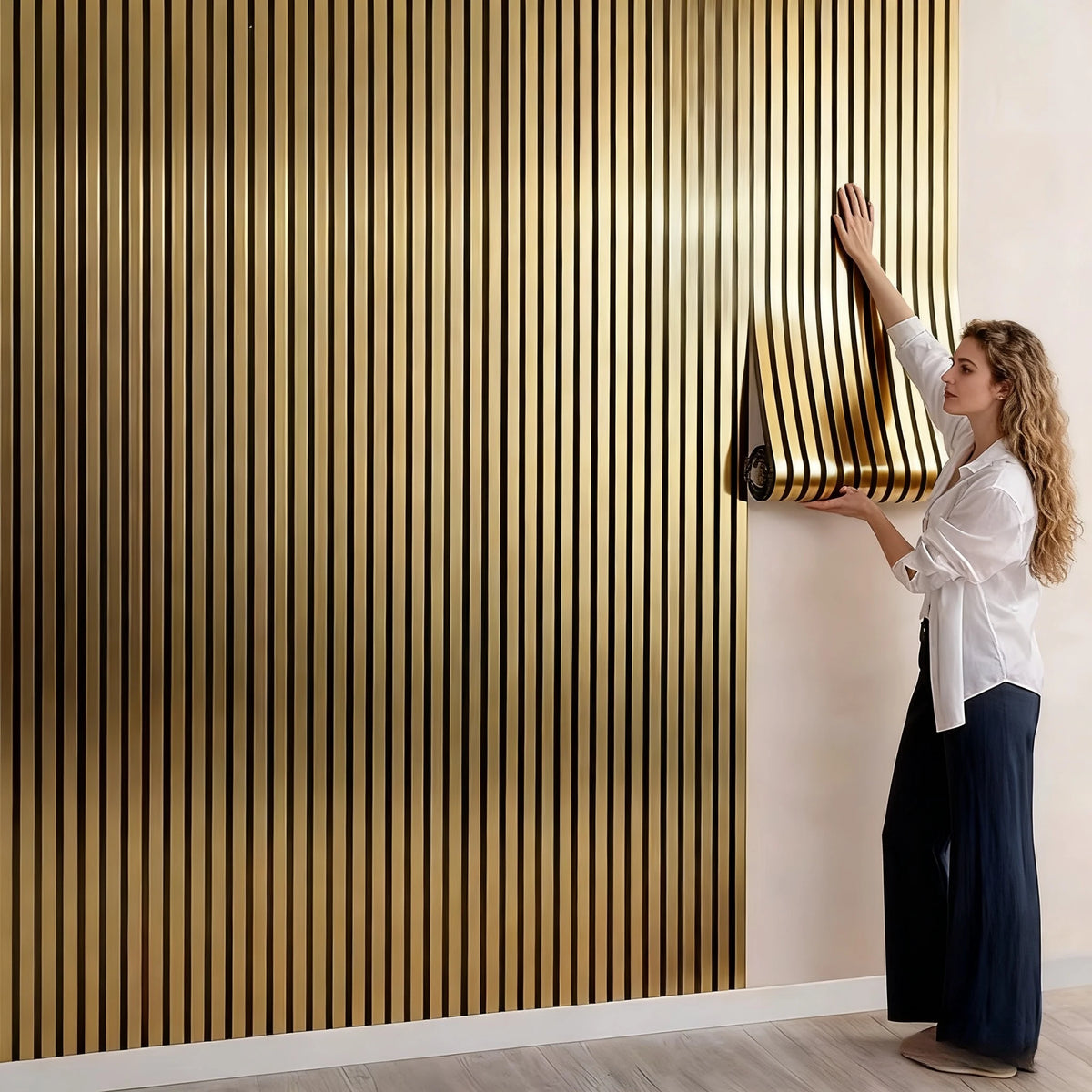 A woman is adjusting a vertical, ribbed gold wallpaper panel on a white wall.