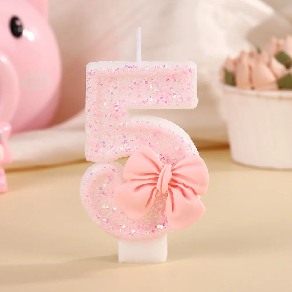 A pink glitter candle shaped like the number 5 with a bow, set against a soft background.