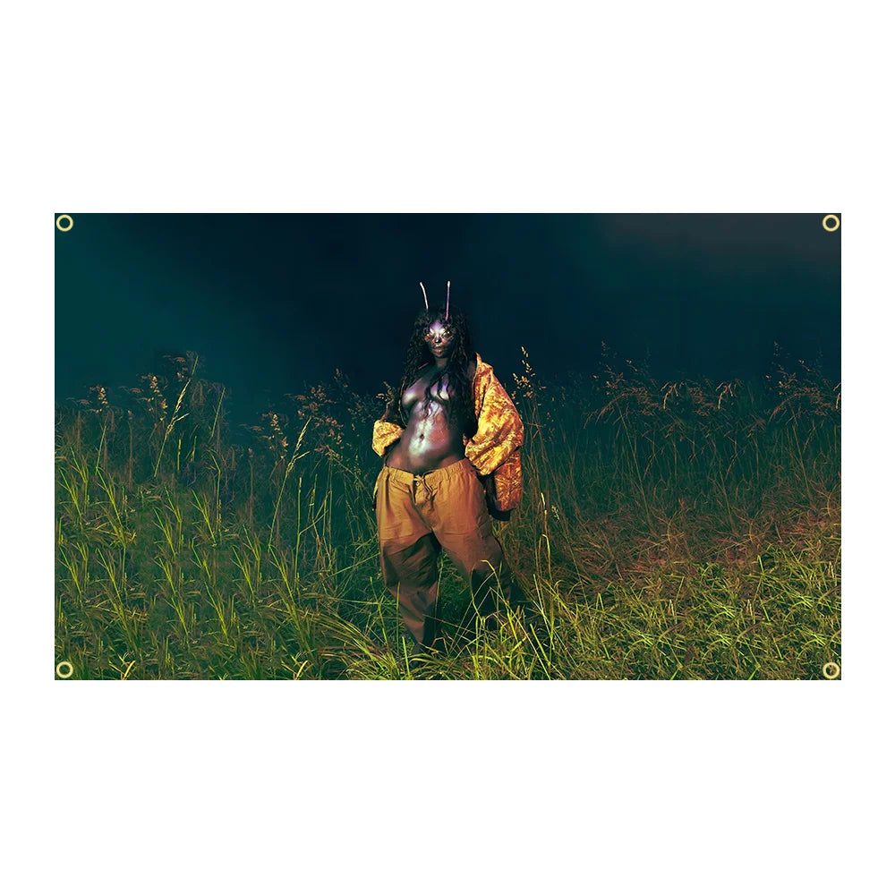 Eine dunkle, stimmungsvolle Aufnahme einer Figur mit langem schwarzem Haar und dunkler Haut, die in hohem grünem Gras steht.
