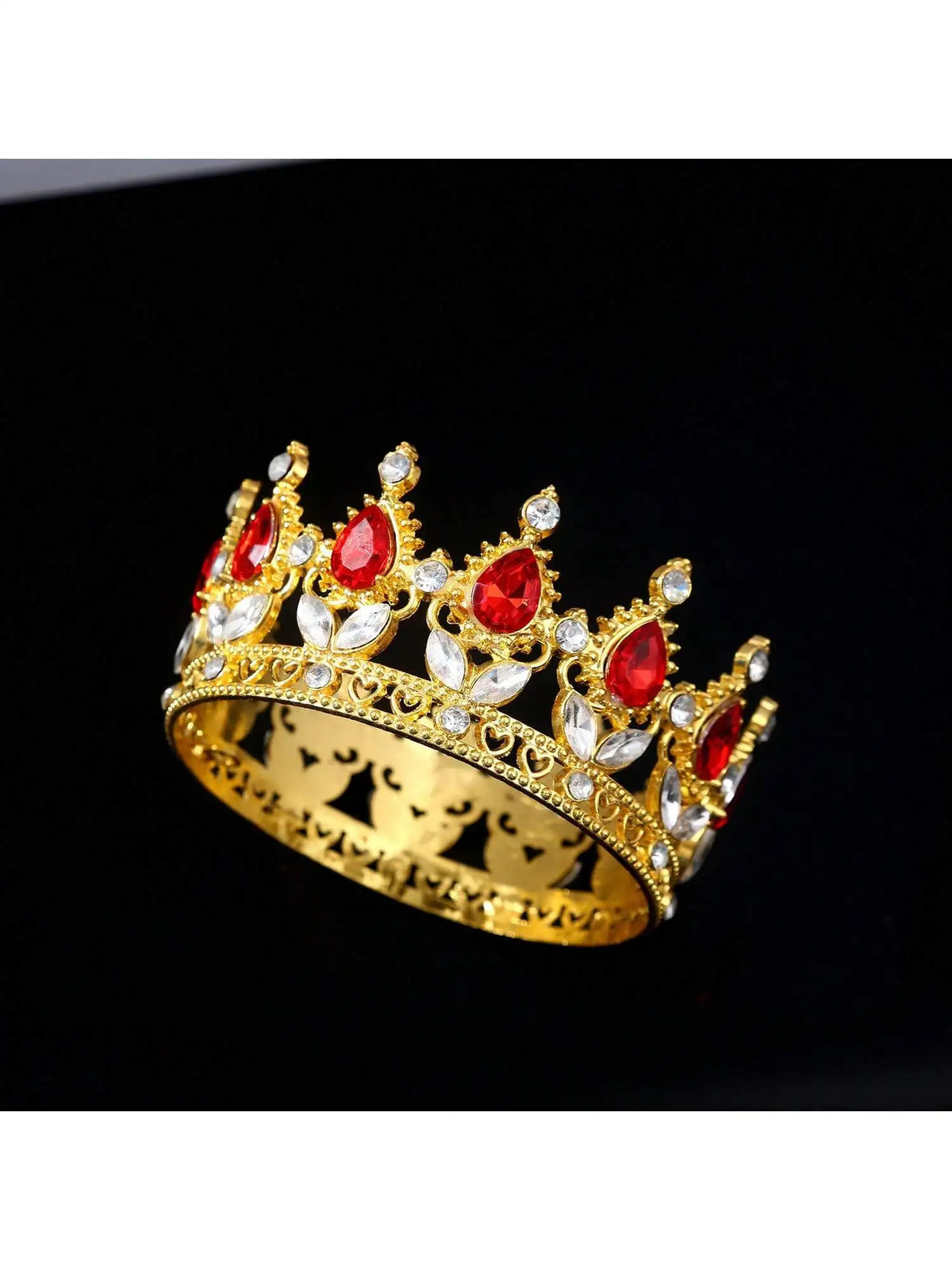 A gold crown featuring red gemstones and clear crystals, used as a cake topper.