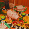 Adorable pink piggy bank with a straw ribbon surrounded by various coins and cupcakes on an orange table.