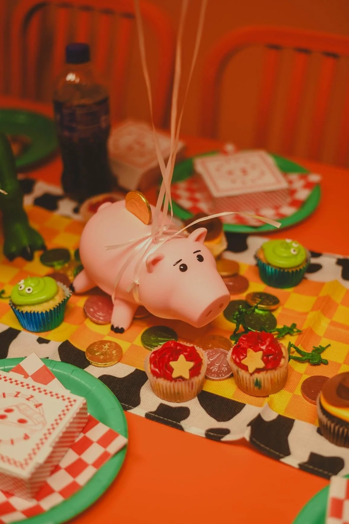 Adorable pink piggy bank with a straw ribbon surrounded by various coins and cupcakes on an orange table.
