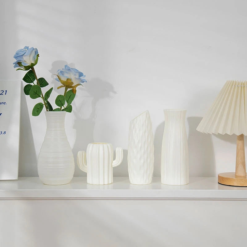 Weiße moderne Plastikblumenvase mit grüner Rose und blauer Blume in weißer Keramik auf einem Regal.