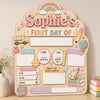 A wooden sign for a child's first day of school featuring illustrations like a school bus, rainbow, and various labels.