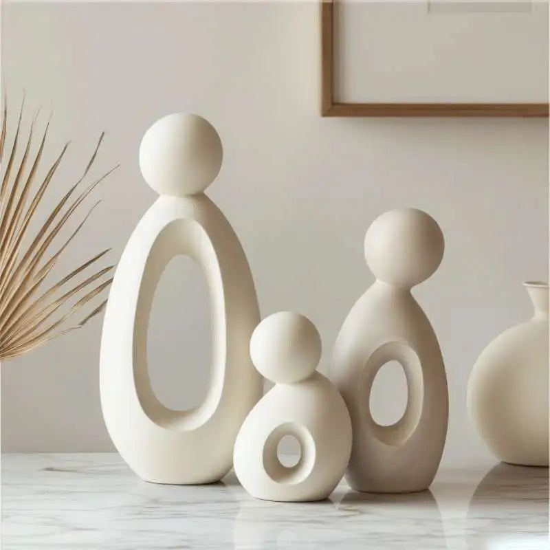 A set of modern white resin family statues depicting a mother, father, and child on a marble surface.