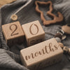 A close-up of wooden baby milestone cards showing the numbers 20 and 05 on a gray fabric background.