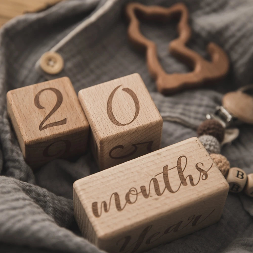 A close-up of wooden baby milestone cards showing the numbers 20 and 05 on a gray fabric background.