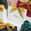 A collection of elegant paperboard thank you gift bags in shades of pink, red, and green with gold ribbon bows.