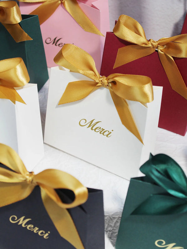 A collection of elegant paperboard thank you gift bags in shades of pink, red, and green with gold ribbon bows.