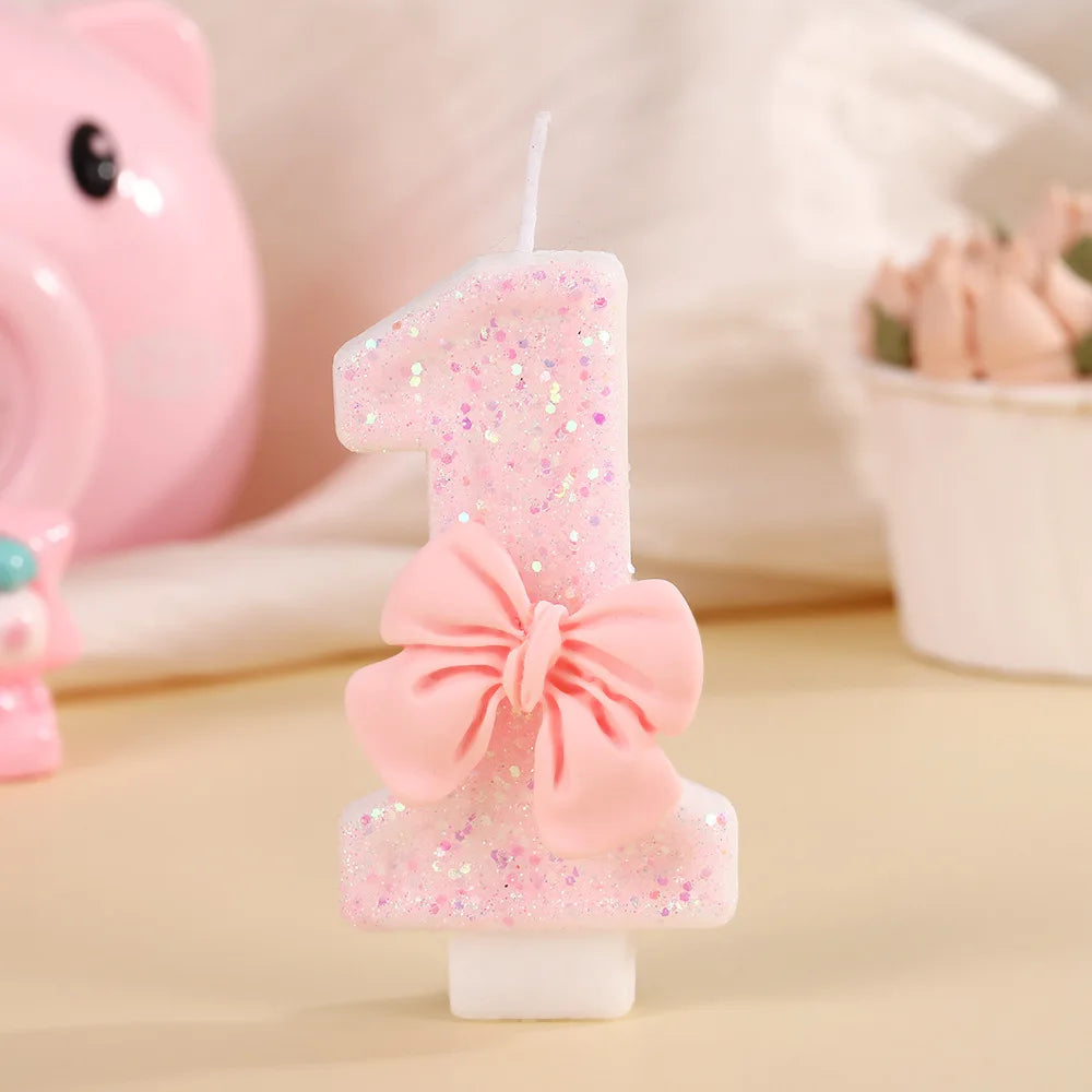 A single pink glitter birthday candle shaped like the number one with a bow on a white stand.