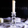 A tall white pillar candle in a clear glass holder resting on a light gray fabric.