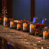 A display of pillar candles in glass holders arranged on a wooden table with seasonal foliage.