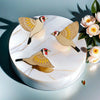 Three vintage wooden bird wall decorations with gold and brown patterns displayed on a white marble cake.