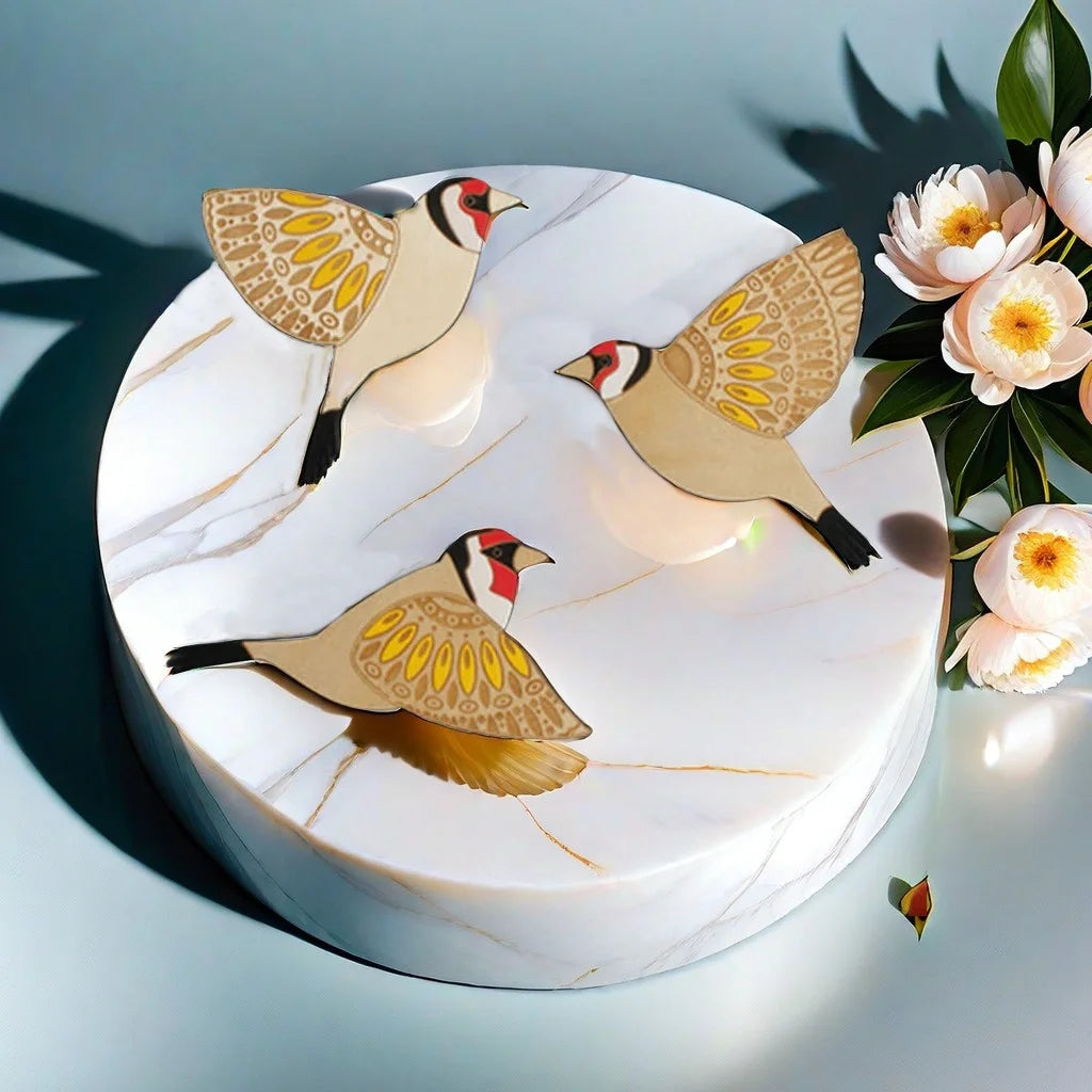 Three vintage wooden bird wall decorations with gold and brown patterns displayed on a white marble cake.