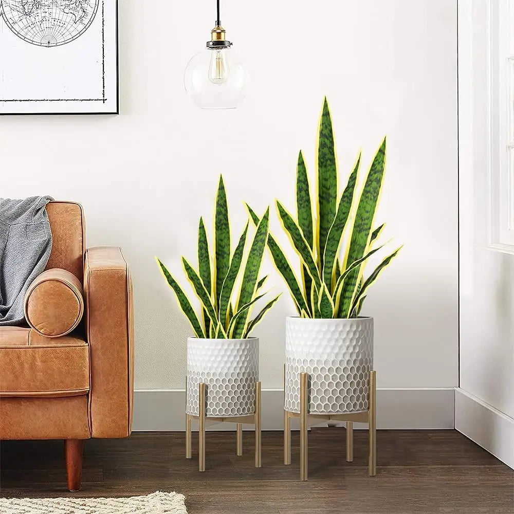 Una planta de serpiente artificial en maceta con hojas verdes largas, sobre un suelo de madera junto a un sillón de cuero.