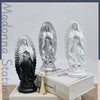 Three resin statues of Our Lady of Guadalupe in silver and white, displayed on a white book.