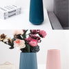 A collection of dried and fresh flowers in various shades of pink, white, and orange arranged in tall, ribbed ceramic vases.