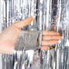 A hand holds metallic silver tinsel foil fringe curtain material.