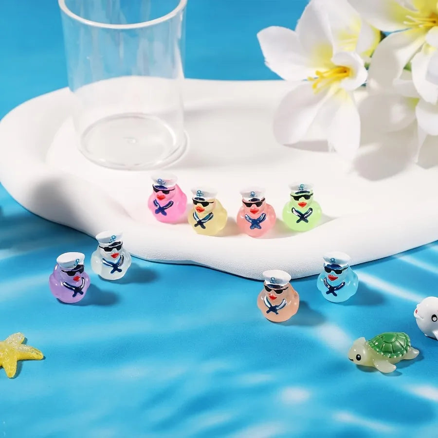A collection of glow-in-the-dark resin cruise duck decorations in various colors arranged on a white platter with a glass cup