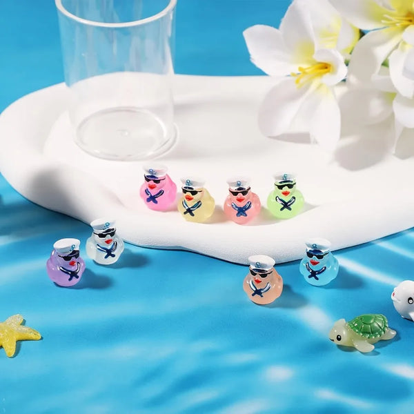 A collection of glow-in-the-dark resin cruise duck decorations in various colors arranged on a white platter with a glass cup
