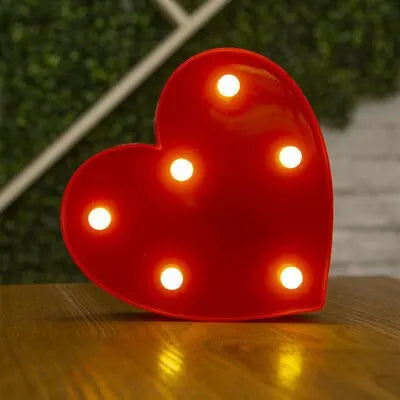 A bright red heart-shaped LED night light with multiple glowing white lights resting on a wooden surface.