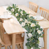 Artificial eucalyptus and rose garland with greenery displayed on a wooden table setting.