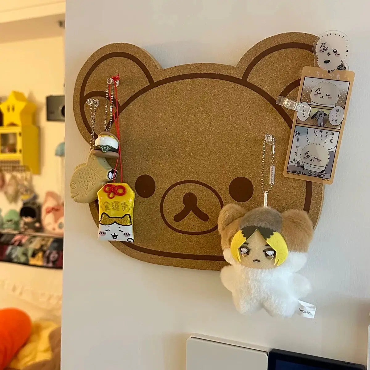 A felt wall decor panel shaped like a brown bear face with large eyes, featuring hanging charms and a felt animal figure.