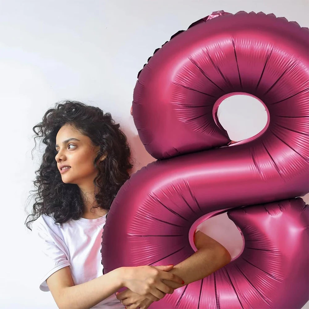 A woman is holding a large, shiny pink foil number balloon shaped like the number 9.
