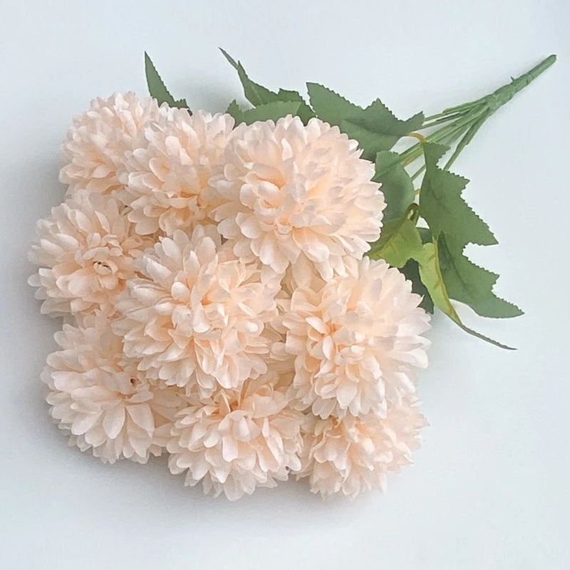 A bouquet of light pink artificial hydrangea and camellia flowers with green leaves.
