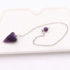 A silver chain necklace with a purple gemstone pendant rests on a white rectangular board.