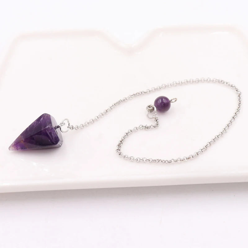 A silver chain necklace with a purple gemstone pendant rests on a white rectangular board.
